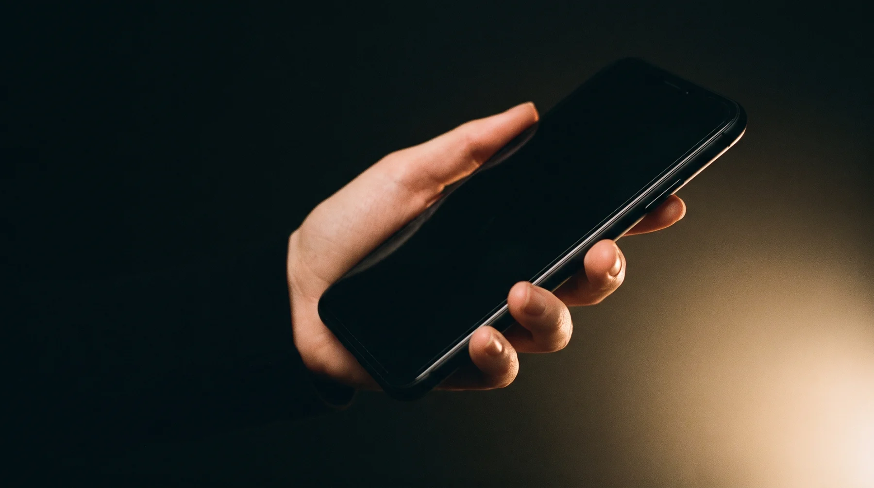 A hand holding a smartphone against a dark background